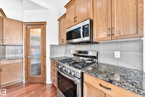 Kitchen featuring light wood cabinetry, granite countertops, stainless steel appliances, a tile backsplash, and wood-finish flooring - 2923 16 Street Nw, Edmonton, AB - Indoor Photo Showing Kitchen