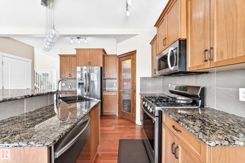 Open-concept kitchen featuring granite countertops, wood cabinetry, stainless steel appliances, and wood-finish flooring - 2923 16 Street Nw, Edmonton, AB - Indoor Photo Showing Kitchen With Double Sink With Upgraded Kitchen