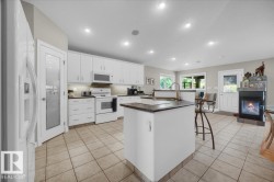 Expansive open-concept kitchen featuring a central island with sink, white cabinetry with under-cabinet lighting, and integrated white appliances - 