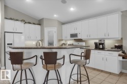 Kitchen featuring white cabinetry with silver hardware, an integrated kitchen island with counter seating, a stainless steel sink with a gooseneck faucet, a white side-by-side refrigerator, and tile flooring - 