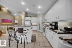 Kitchen featuring white cabinetry with silver-toned hardware, a tile backsplash, and a pantry with a frosted glass door - 