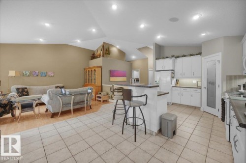 Open-concept living area and kitchen featuring vaulted ceilings, recessed lighting, tile flooring, white cabinetry, and a kitchen island with seating - 928 Thompson Place Nw, Edmonton, AB - Indoor Photo Showing Kitchen