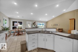 Kitchen featuring white cabinetry, dark countertops, a double basin sink, and a built-in dishwasher - 