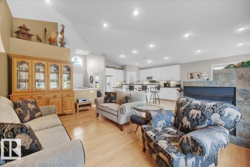 Spacious open-concept living area featuring wood-finish flooring, a stone-clad fireplace, and vaulted ceilings with recessed lighting - 928 Thompson Place Nw, Edmonton, AB - Indoor Photo Showing Living Room