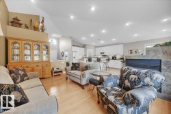 Spacious open-concept living area featuring wood-finish flooring, a stone-clad fireplace, and vaulted ceilings with recessed lighting - 