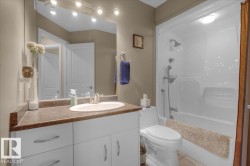 Full bathroom featuring a white vanity with an integrated sink, a dark countertop, white cabinetry with curved hardware, and a combination bathtub and shower with a single-handle faucet - 