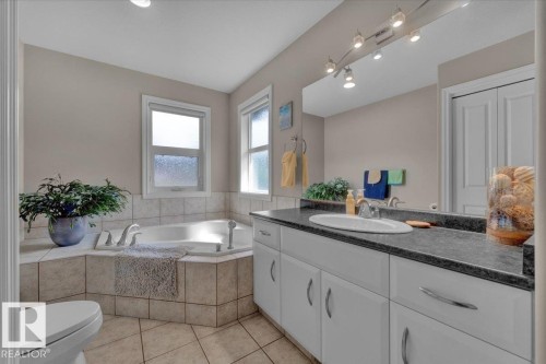Bathroom featuring a built-in corner soaking tub with tile surround, a double-door closet, a vanity with a dark countertop and integrated sink, and track lighting above the mirror - 928 Thompson Place Nw, Edmonton, AB - Indoor Photo Showing Bathroom