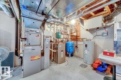 Utility room featuring forced air furnace, hot water heater, water treatment system, and exposed ductwork - 
