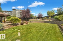 Expansive backyard featuring a manicured lawn, tiered retaining walls, mature trees, a covered patio, and stepping stones - 
