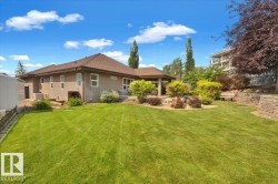 Expansive green lawn with a stucco exterior home featuring a covered patio, tiered landscaping with mature shrubs, and a stone retaining wall - 