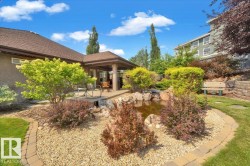 Expansive outdoor living area featuring a covered patio, a rock garden with a built-in pond, mature landscaping, and a manicured lawn - 