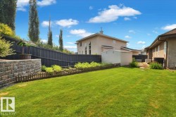 Expansive backyard featuring a lush lawn, a stone retaining wall, and a black privacy fence - 