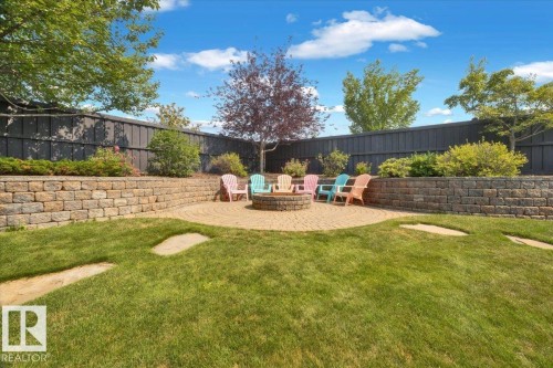 Expansive backyard featuring a circular paver patio with a built-in fire pit, surrounded by tiered stone retaining walls and mature landscaping - 928 Thompson Place Nw, Edmonton, AB - Outdoor With Backyard