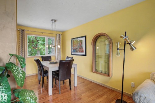 Hardwood flooring throughout featuring a window with abundant natural illumination, a contemporary chandelier, and an arched stained-glass window accent - 9516 129A Avenue Nw, Edmonton, AB - Indoor Photo Showing Dining Room
