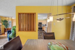 Dining area featuring a contemporary linear chandelier with frosted glass shades, a wood-finish dining table, and direct sightlines to the kitchen - 