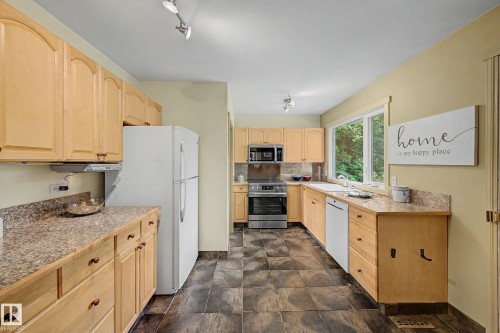 Kitchen featuring light wood cabinetry, stone-look countertops, stainless steel appliances, and dark tile flooring - 9516 129A Avenue Nw, Edmonton, AB - Indoor Photo Showing Kitchen