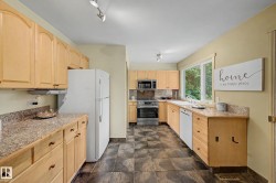 Kitchen featuring light wood cabinetry, stone-look countertops, stainless steel appliances, and dark tile flooring - 