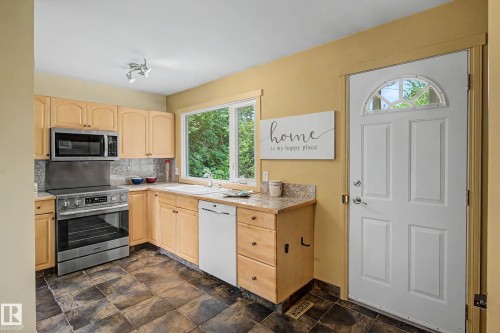 Kitchen featuring natural wood-finish cabinetry, stainless steel range and microwave, light-toned countertop, and dark-toned floor tiles - 9516 129A Avenue Nw, Edmonton, AB - Indoor Photo Showing Kitchen