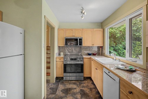 Kitchen featuring wood cabinetry, stone countertops, a stainless steel range, and a large window - 9516 129A Avenue Nw, Edmonton, AB - Indoor Photo Showing Kitchen With Double Sink