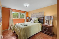 Bedroom featuring warm-toned walls, wood-finish flooring, a contemporary ceiling light fixture, and a window with exterior tree views - 
