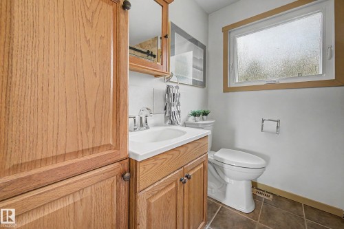 Bathroom featuring a wood-finish vanity with a white countertop and integrated sink, a white toilet, and a window with wood-finish trim - 9516 129A Avenue Nw, Edmonton, AB - Indoor Photo Showing Bathroom