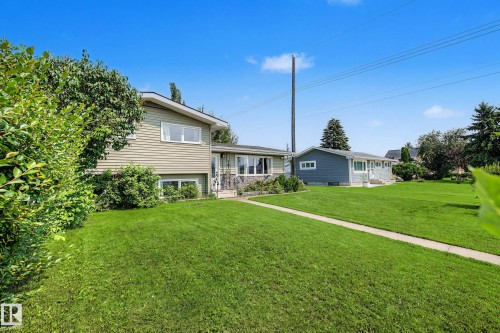 Expansive green lawn with a concrete pathway leading to a split-level residence featuring light-colored siding and a stone facade accent - 9516 129A Avenue Nw, Edmonton, AB - Outdoor