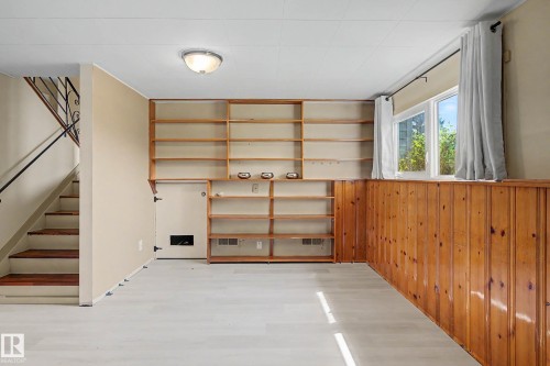 Lower-level living area featuring light wood-finish flooring, built-in shelving, wood paneling, and a window for natural light - 9516 129A Avenue Nw, Edmonton, AB - Indoor Photo Showing Other Room