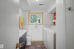 Bathroom featuring a vanity with dark cabinetry and chrome hardware, a toilet, and a window with wood trim - 