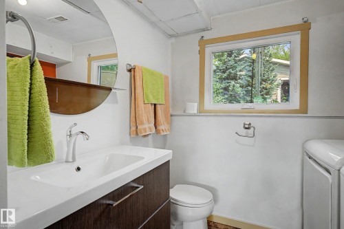 Bathroom featuring a contemporary vanity with an integrated sink, polished chrome faucet, and a round wall-mounted mirror - 9516 129A Avenue Nw, Edmonton, AB - Indoor Photo Showing Bathroom