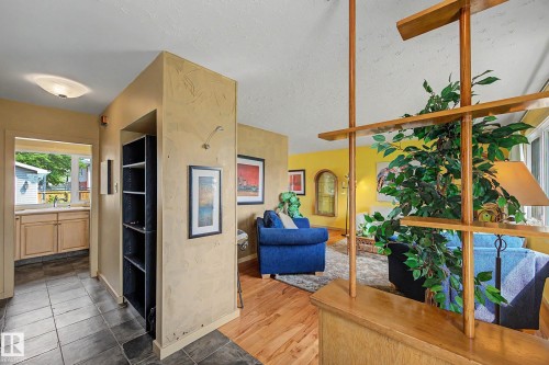 Open concept interior featuring light wood-finish flooring, a built-in room divider, and an entryway with dark tile flooring - 9516 129A Avenue Nw, Edmonton, AB - Indoor Photo Showing Other Room
