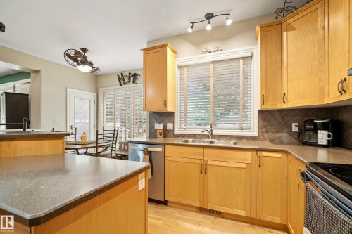 Kitchen featuring light wood cabinetry, stone-look countertops, stainless steel appliances, and a double basin sink beneath a window with blinds - 416 Sparling Crest Sw, Edmonton, AB - Indoor Photo Showing Kitchen With Double Sink