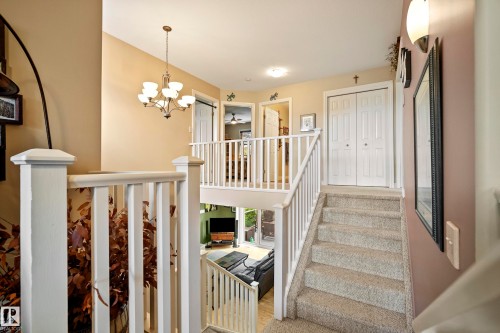 Multi-level interior featuring a carpeted staircase with white railings, white paneled bifold doors, and a decorative chandelier - 416 Sparling Crest Sw, Edmonton, AB - Indoor Photo Showing Other Room