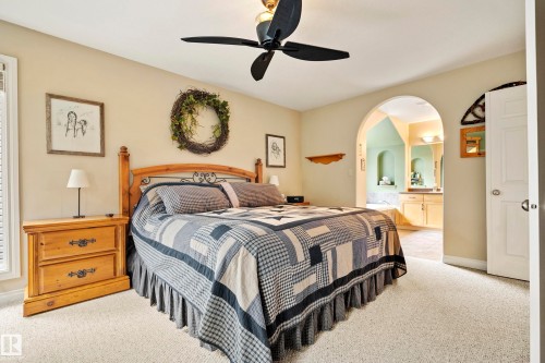 Spacious bedroom with light-colored carpeting, a black ceiling fan, and an arched doorway leading to a bathroom with tile flooring and a double vanity - 416 Sparling Crest Sw, Edmonton, AB - Indoor Photo Showing Bedroom