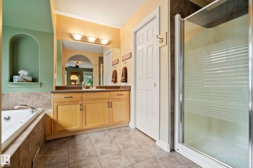Bathroom with a built-in jetted tub, a separate shower enclosure with frosted glass, a light wood-finish vanity with dual sinks, and tile flooring - 416 Sparling Crest Sw, Edmonton, AB - Indoor Photo Showing Bathroom