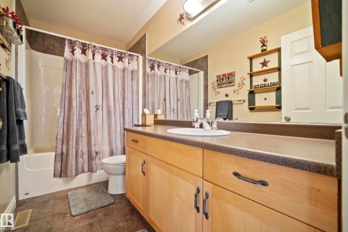 Bathroom featuring a bathtub with an integrated shower, a light wood-finish vanity with ample storage, a solid surface countertop, and a single basin sink - 416 Sparling Crest Sw, Edmonton, AB - Indoor Photo Showing Bathroom