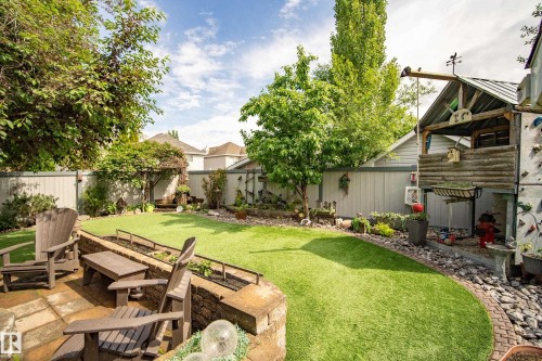 Spacious backyard featuring a stone patio, manicured lawn, built-in planters with stone retaining walls, privacy fencing, and mature trees - 416 Sparling Crest Sw, Edmonton, AB - Outdoor With Backyard
