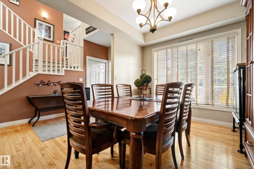 Formal dining area featuring hardwood flooring, a large window with horizontal blinds, and a brass chandelier - 416 Sparling Crest Sw, Edmonton, AB - Indoor Photo Showing Dining Room