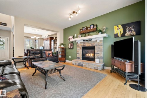Living area featuring a stone-clad fireplace with a white mantel, light wood-finish flooring, recessed lighting, and an open entryway to an adjacent dining space - 416 Sparling Crest Sw, Edmonton, AB - Indoor Photo Showing Living Room With Fireplace