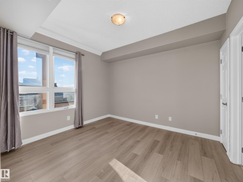 Spacious room with modern wood-finish flooring, neutral wall tones, and white baseboards - #1208 9939 109 St Nw, Edmonton, AB - Indoor Photo Showing Other Room