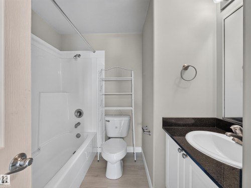 Bathroom featuring a white bathtub with a shower, a toilet, a vanity with a dark countertop and white cabinetry, and wood-finish flooring - #1208 9939 109 St Nw, Edmonton, AB - Indoor Photo Showing Bathroom