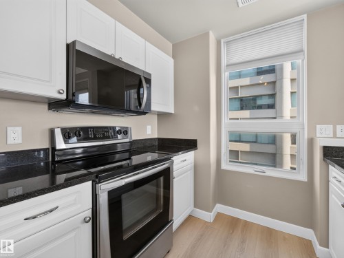 Contemporary kitchen featuring white cabinetry, dark granite countertops, stainless steel appliances, and wood-finish flooring - #1208 9939 109 St Nw, Edmonton, AB - Indoor Photo Showing Kitchen