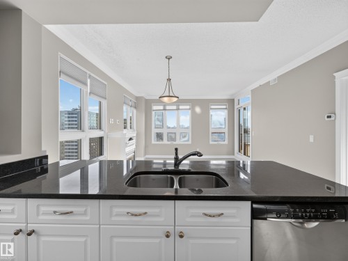 Kitchen island with a dark countertop and undermount double basin sink - #1208 9939 109 St Nw, Edmonton, AB - Indoor Photo Showing Kitchen With Double Sink