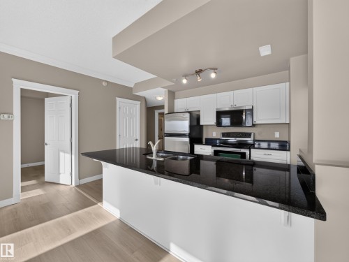 Contemporary kitchen featuring an expansive black countertop island with undermount sink, white cabinetry, and stainless steel appliances - #1208 9939 109 St Nw, Edmonton, AB - Indoor Photo Showing Kitchen With Stainless Steel Kitchen