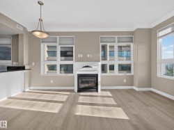 Spacious living area featuring light wood-finish flooring, a decorative fireplace with a white mantel, and multiple windows with blinds - 