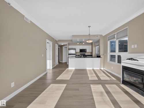 Open-concept living area featuring light wood-finish flooring and a built-in fireplace - #1208 9939 109 St Nw, Edmonton, AB - Indoor With Fireplace