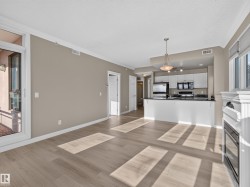 Open-concept living space featuring wood-finish flooring, a white trim fireplace, and a kitchen with white cabinetry, dark countertops, and stainless steel appliances - 
