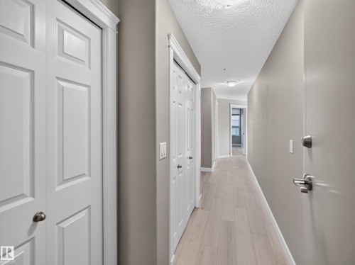 Hallway with light wood-finish flooring, neutral wall paint, and multiple white panel doors - #1208 9939 109 St Nw, Edmonton, AB - Indoor Photo Showing Other Room