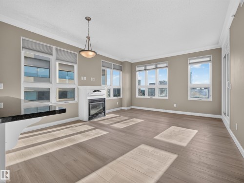 Spacious living area featuring light wood-finish flooring, a white mantel fireplace, and a black countertop bar - #1208 9939 109 St Nw, Edmonton, AB - Indoor Photo Showing Living Room With Fireplace
