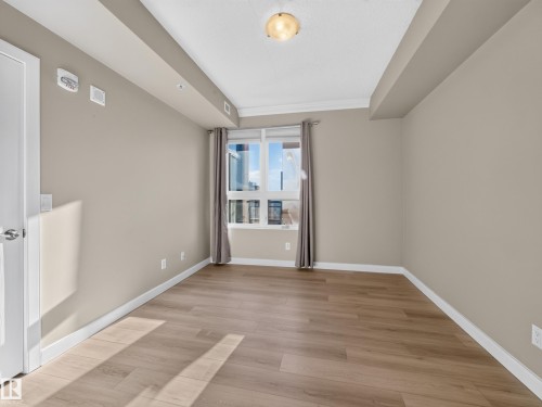 Spacious room featuring wood-finish flooring, neutral-toned walls, a large window, and white trim - #1208 9939 109 St Nw, Edmonton, AB - Indoor Photo Showing Other Room