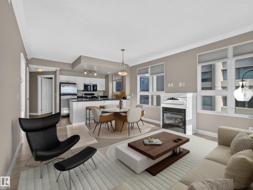 Open-concept living space featuring wood-finish flooring, a contemporary fireplace with a white mantel, and multiple windows - #1208 9939 109 St Nw, Edmonton, AB - Indoor Photo Showing Living Room With Fireplace